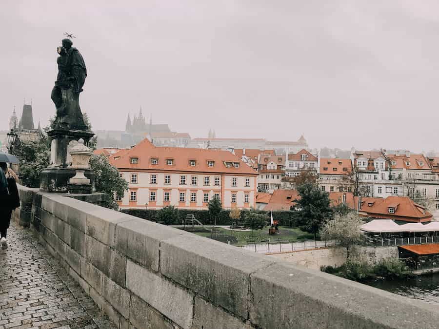 Side of the Charles Bridge with a gothic statue and the city in the distance