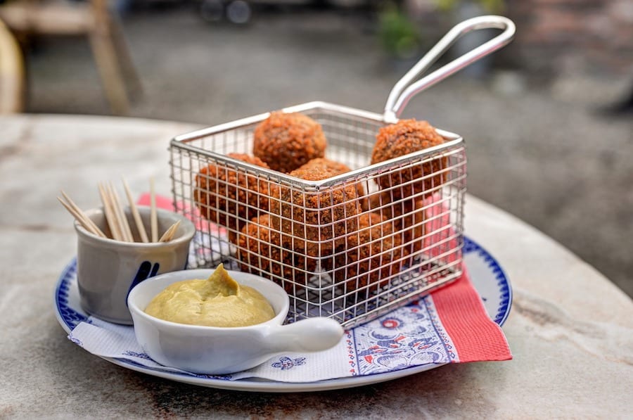 Round, fried balls in a container with mustard on the side 