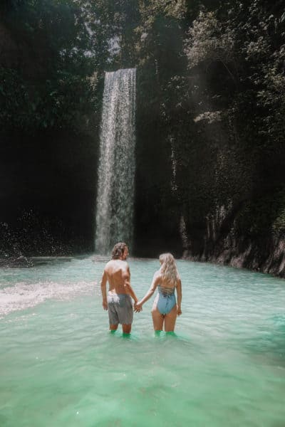 Two people holding hands in front of a waterfall