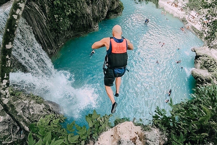 Man jumping into the water from the top of a waterfall