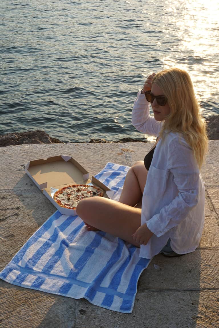 Girl eating pizza on pier in Herceg Novi Montenegro and enjoying sunset.