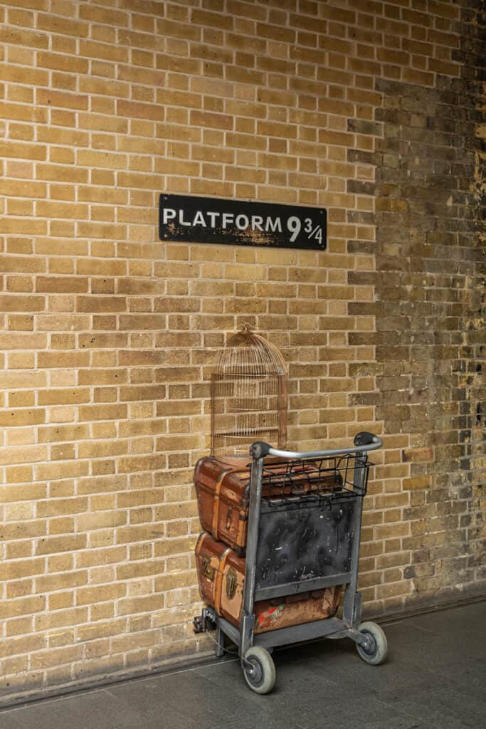 London, Great Britain - July 3, 2022: Platform, 9 3/4 at King's Cross railway station is a fake set-up out of Harry Potter movies. Beige brick wall and half luggage wheeler crashing into it.
