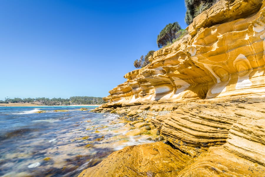 Amazing coast line called Painted Cliffs with orange yellow colored sand limestone rocks and geology structures at shore, perfect expedition on warm sunny clear day, Maria Island, Tasmania, Australia