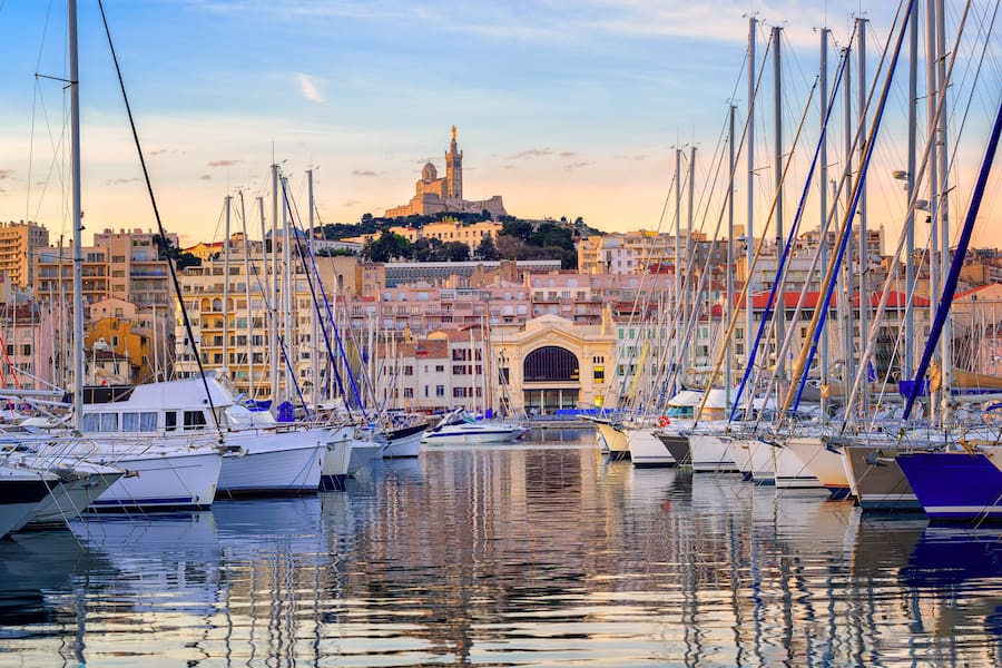 Yachts reflecting in the still water of the old Vieux Port of Marseilles beneath Cathedral of Notre Dame, France, on sunrise