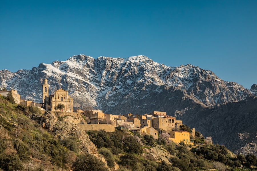 Mountain village of Montemaggiore in the Balagne region of Corsica with a snow capped Monte Grosso mountain behind and clear blue sky