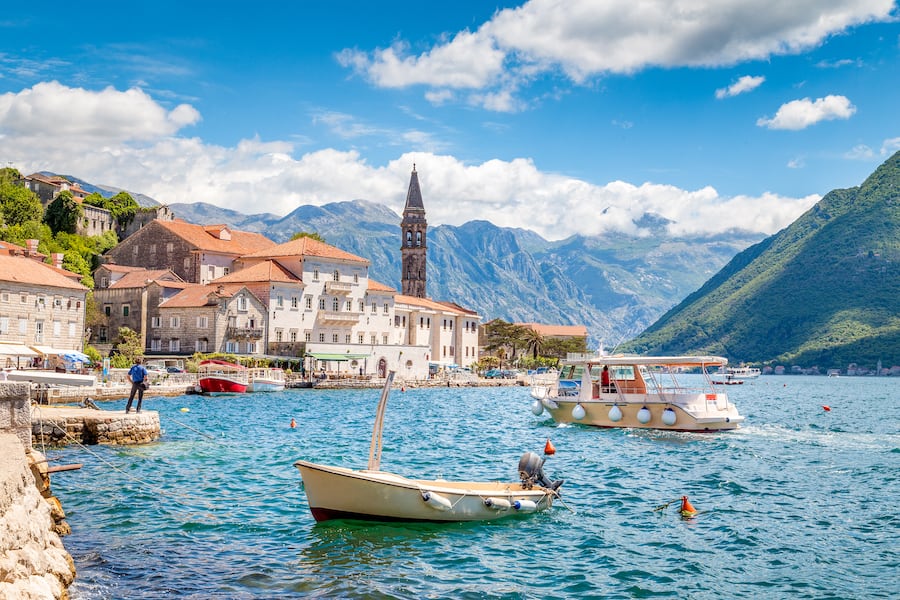 Scenic panorama view of the historic town of Perast at famous Bay of Kotor with boats on a beautiful sunny day with blue sky and clouds in summer, Montenegro, southern Europe