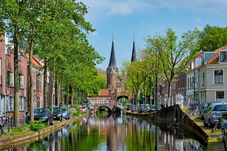 Picturesque Delft cityscape view with Eastern Gate Oostport and canal with cars and bicycles parked along. Delft, Netherlands's