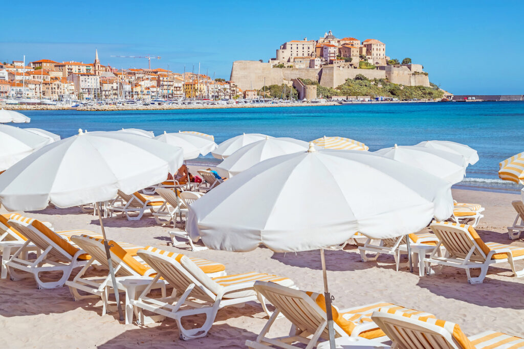 Sandy Corsican beach and amazing azure sea with an ancient citadel of Calvi in background. Historical touristic place.